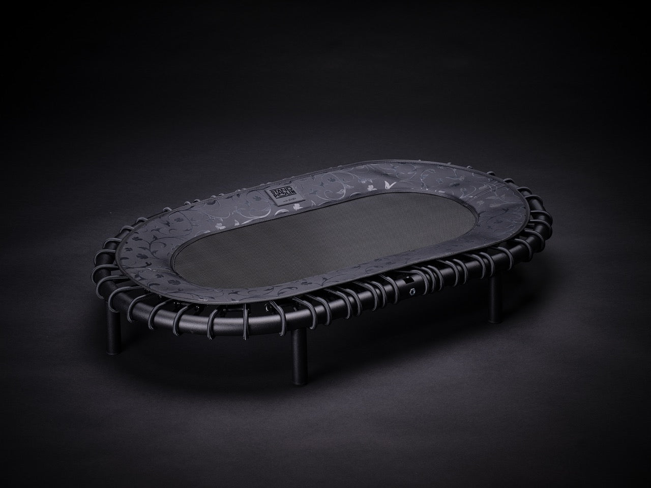 Standpolin in Schwarz mit floraler Musterung, dunkler Sprungfläche, schwarzem Rahmen und Seilringen für aktives Stehen, Balance und ergonomische Bewegung.